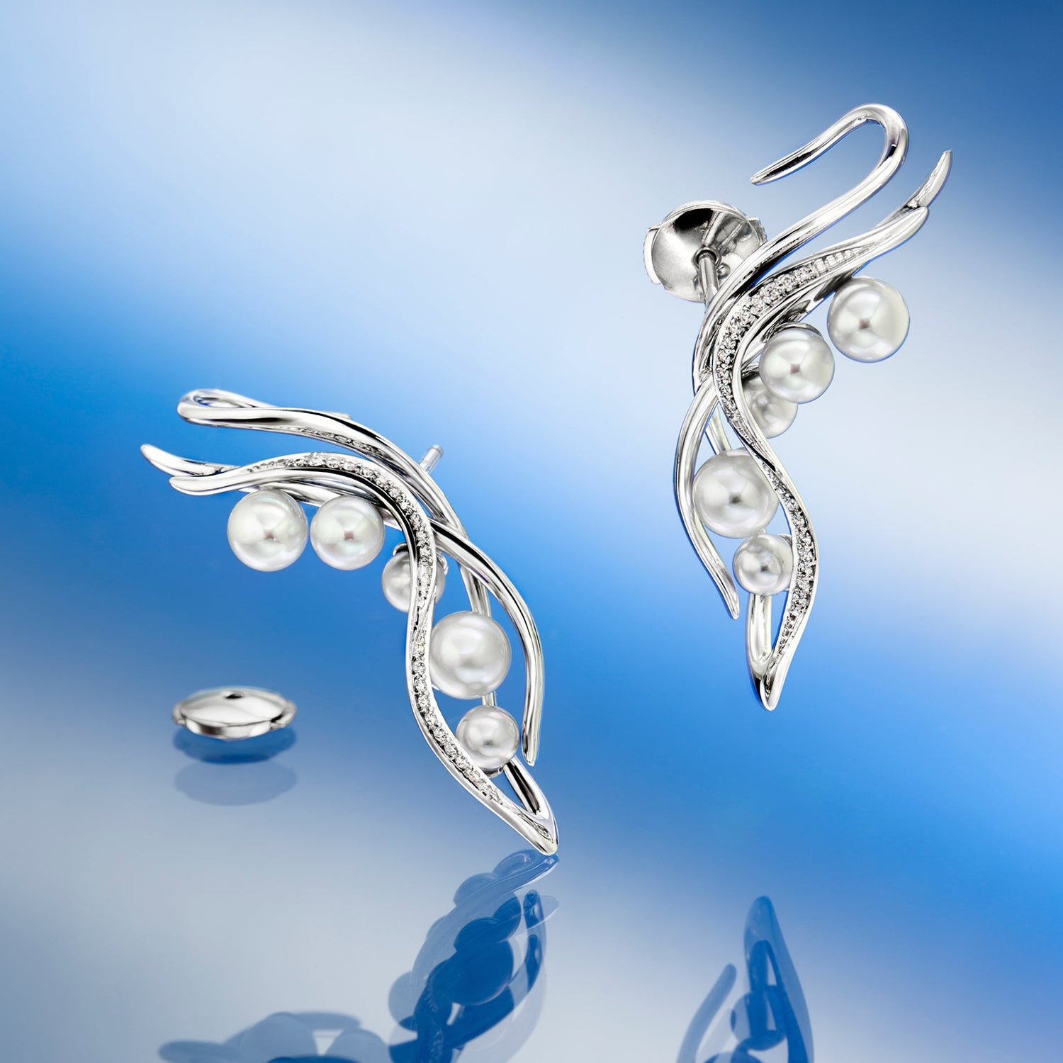 Silver earrings with pearls on a reflective surface