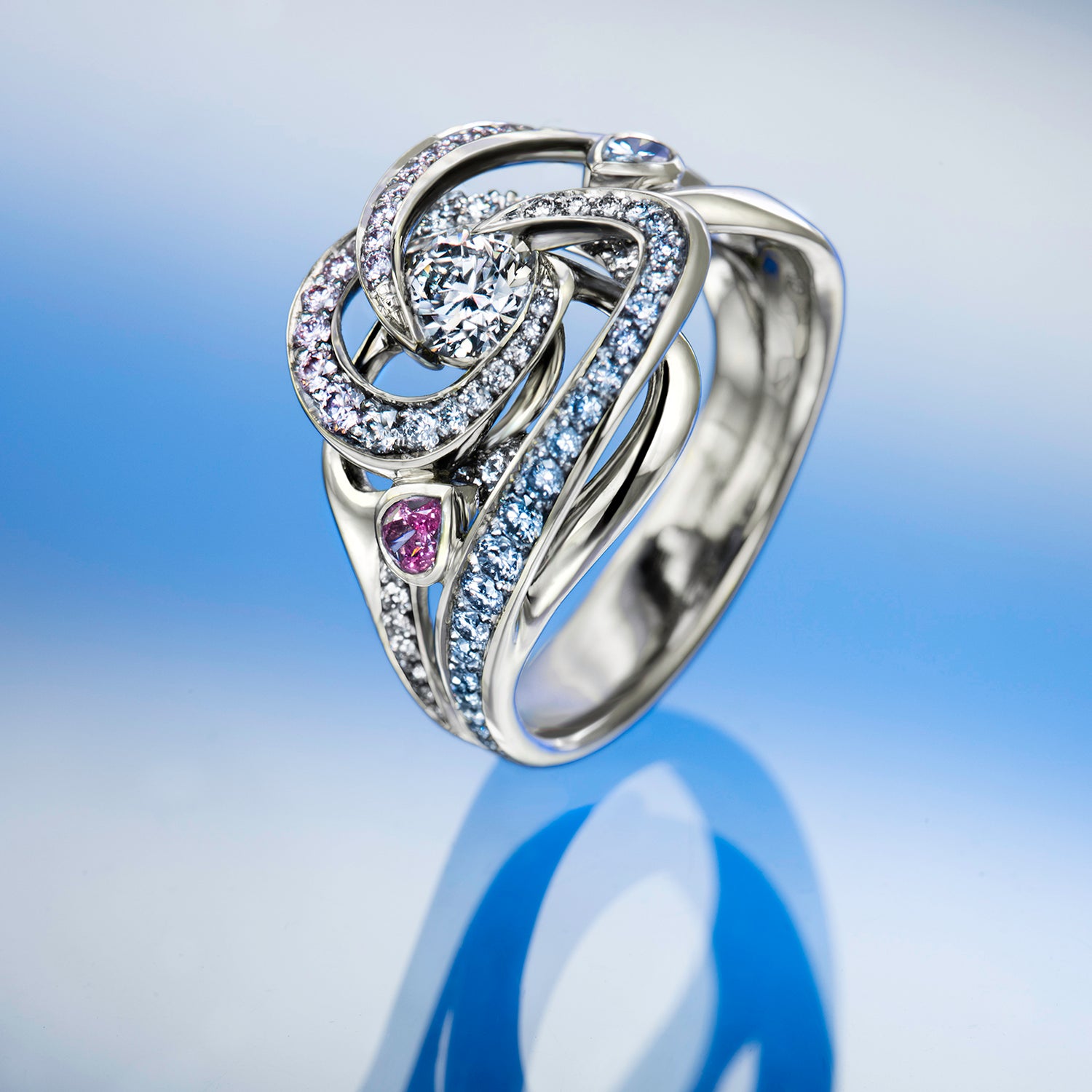 Silver ring with intricate design and gemstones on a reflective surface